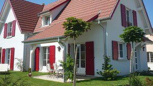 A two-story house with a red roof, white walls, and red shutters. There is a small patio with a table and chairs. - Charming house for 6 people in EGUISHEIM - Gîte HIRONDELLE (Eguisheim)