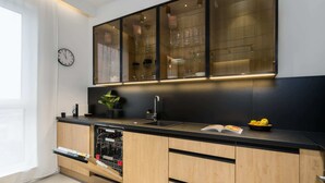 A modern kitchen with wooden cabinets, a black countertop, a dishwasher, and a glass-fronted cabinet above the sink.