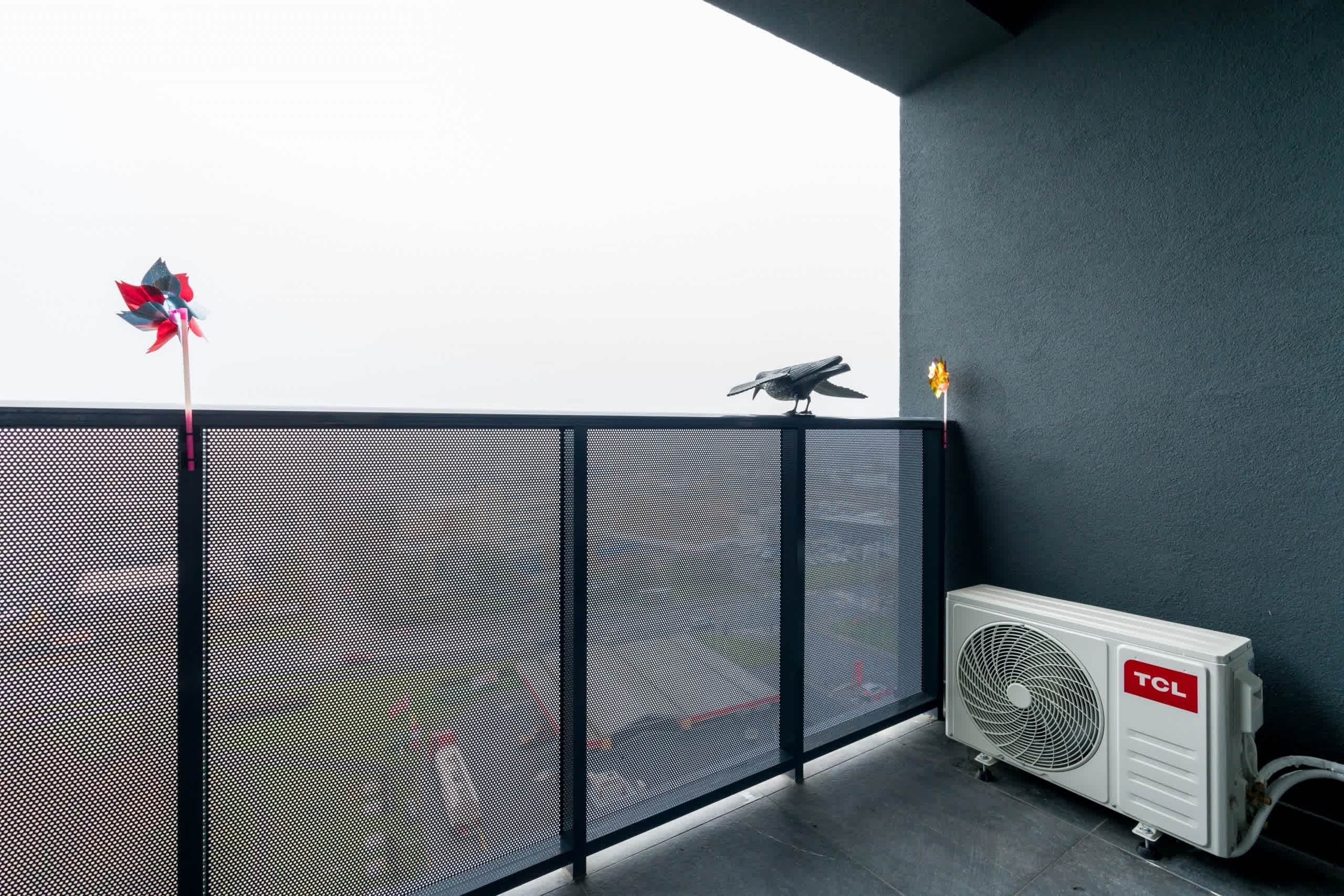 A balcony with a mesh railing, a bird, a pinwheel, and an air conditioning unit.