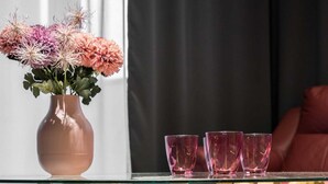 A glass-top coffee table with a unique wooden base, a vase with flowers, and three glasses on the table.