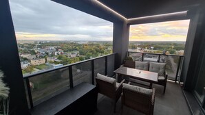 A balcony with a table and chairs, offering a view of a cityscape during sunset.