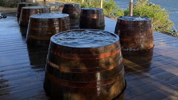 Wooden barrels arranged on a wooden deck with a view of the sea.