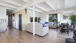 A spacious living area with a sofa, dining table, and chairs. There is a kitchen area with cabinets and a refrigerator.