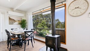 A dining area with a table set for four, a black wood-burning stove, and a large window with a view of trees.