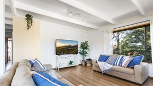 A modern living room with two sofas, a TV, and a large window with a view of greenery.