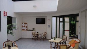 A spacious indoor area with a high ceiling, a flat-screen TV mounted on the wall, and a dining area with wicker furniture.