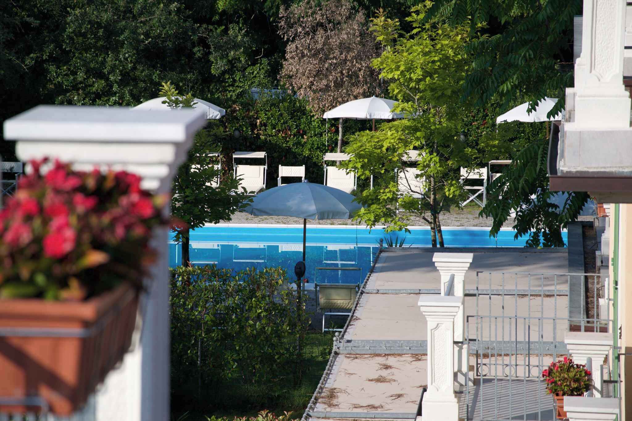 Zona de piscina con sillones blancos y sombrillas, rodeada de vegetación y un muro de piedra.
