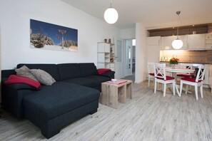 En moderne stue med en mørkegrå sofa, et lille træsofabord og et spiseområde med hvide stole og et bord.