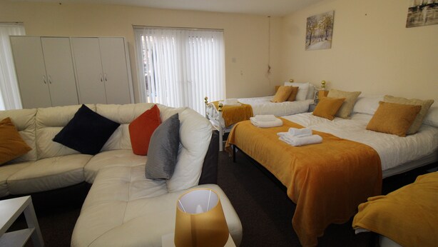 A hotel room with a sofa, two beds, a lamp, and a window with blinds. - Annex St Ann's (Rotherham)