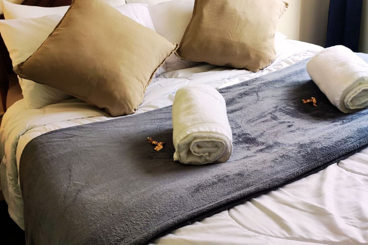 Ein ordentlich bezogenes Bett mit einer grauen Decke, zwei beigen Kissen und einem Holzkopfteil.
