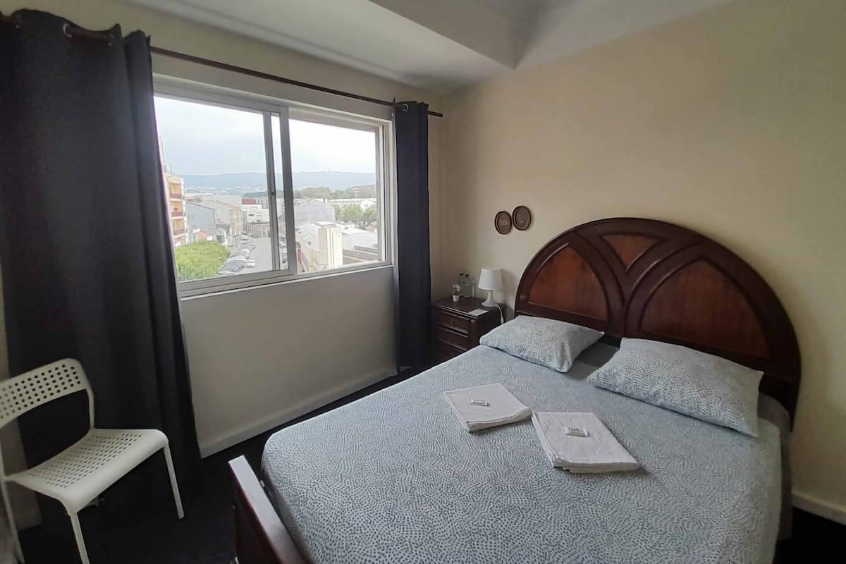 Ein Hotelzimmer mit einem großen Bett, einem kleinen Nachttisch, einem Sessel und einem Fenster mit Blick auf die Stadt.