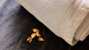 Et hvidt, sammenrullet håndklæde på en mørk stofoverflade med enkelte guldfarvede genstande i nærheden.