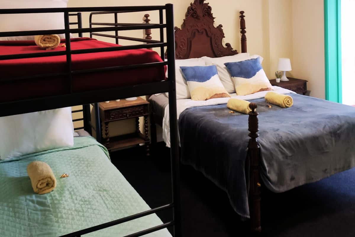 Ein Hotelzimmer mit zwei Etagenbetten, einem Einzelbett und einem Nachttisch mit Lampe.