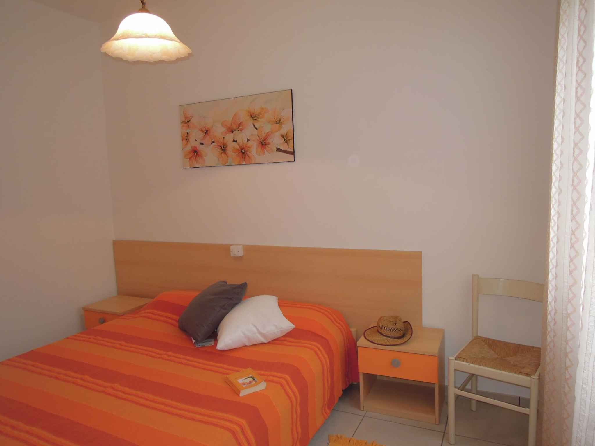 Une chambre à coucher comprenant un lit, une table de chevet, une chaise, une lampe suspendue et un tableau représentant des fleurs.