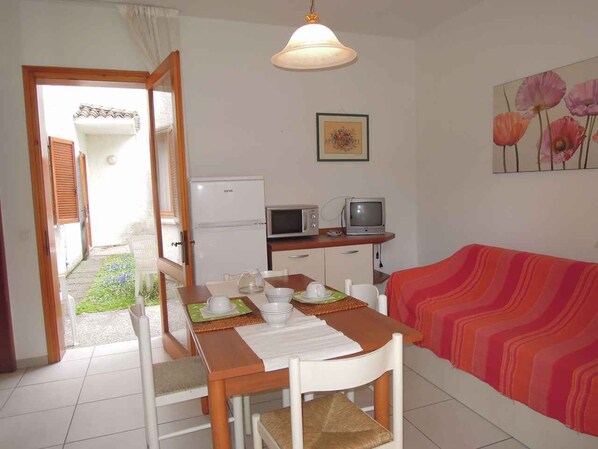 A room with a dining table set for two, a microwave, a television, and a sofa with a striped blanket.