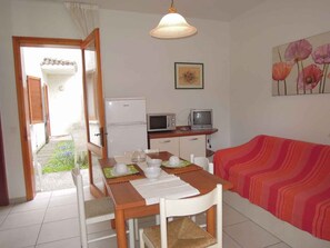 A room with a dining table set for two, a microwave, a television, and a sofa with a striped blanket.