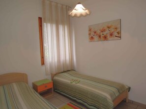 A bedroom with two single beds, a nightstand, a hanging light fixture, and a floral painting on the wall.