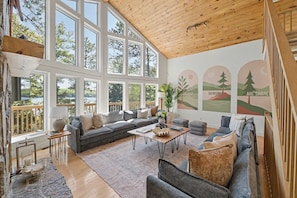 A spacious living room with a large window, a wooden ceiling, and a mural on the wall.