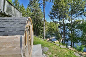 A wooden cabin with a large wooden wheel window, surrounded by trees and a lake.