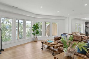 A spacious living room with large windows, a leather sofa, a coffee table, and a potted plant.