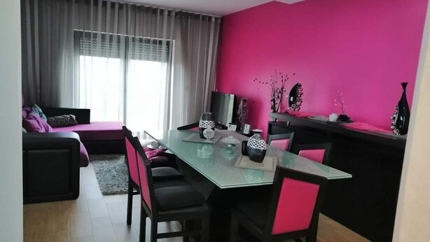 A dining area with a glass table, black chairs, and a pink wall. - Casa Pinheiro 5 minutes from Barcelos city center (Arcozelo)