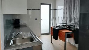 A modern kitchen with a stainless steel sink, a wooden table with a black cloth, and a sliding glass door leading to a balcony. - Casa Pinheiro 5 minutes from Barcelos city center (Arcozelo)