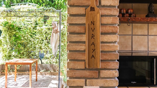 A wooden sign with 'NURAYA' on a brick wall, a wooden table, and a metal rack with baskets. - Villa 'Nuràya' with Sea View and Private Terrace (Capoterra)