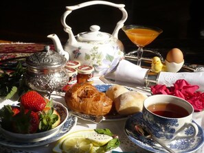 A breakfast setting with a teapot, croissants, strawberries, a glass of orange juice, and a cup of tea.