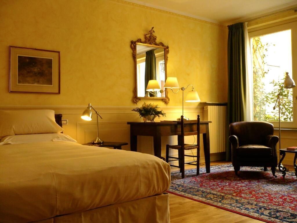 Een hotelkamer met een bed, een bureau met lamp, een stoel en een grote spiegel aan de muur.