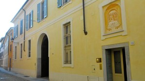 A yellow building with a large arched doorway, a door with a number, and a window with bars. - Relais Vimercati (Crema)