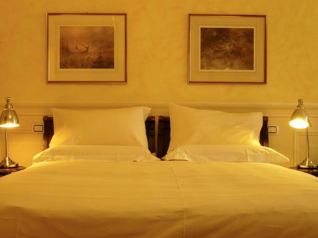 Quarto de hotel com uma cama grande, duas luminárias de cabeceira e duas molduras na parede.