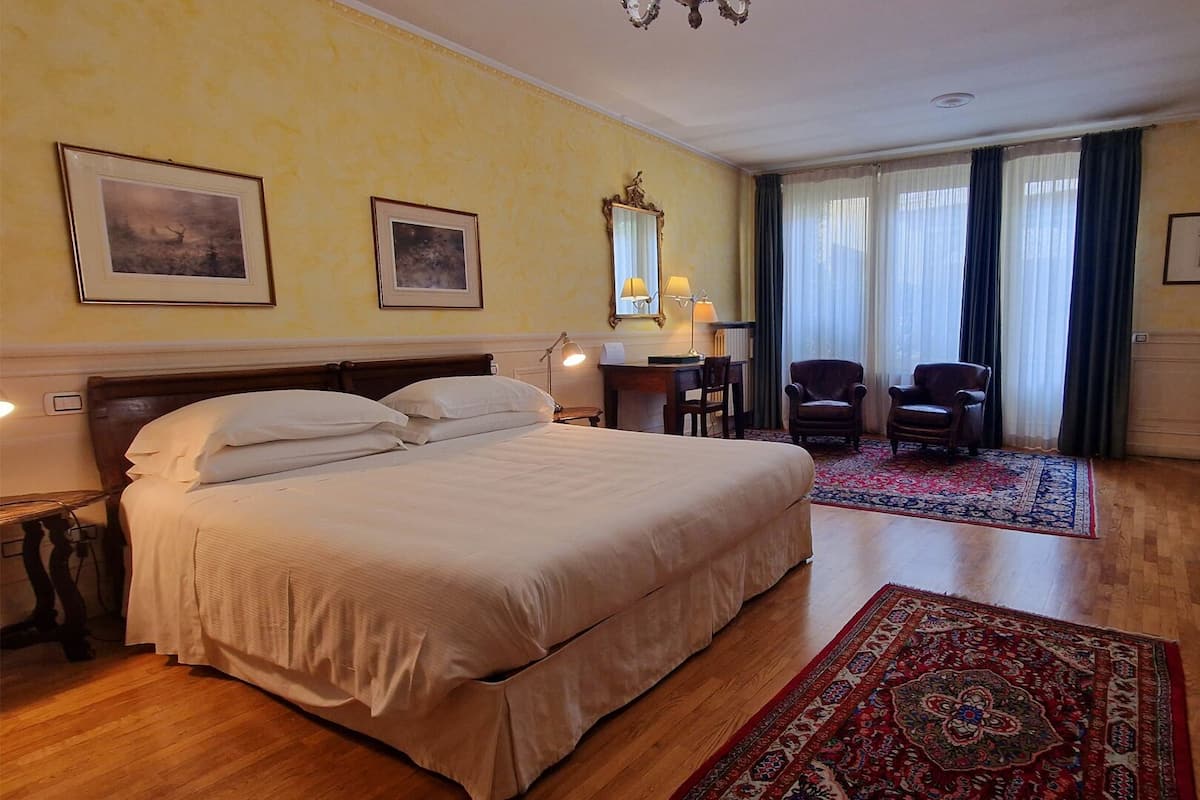 A hotel room with a large bed, two chairs, a desk, and a window with curtains.