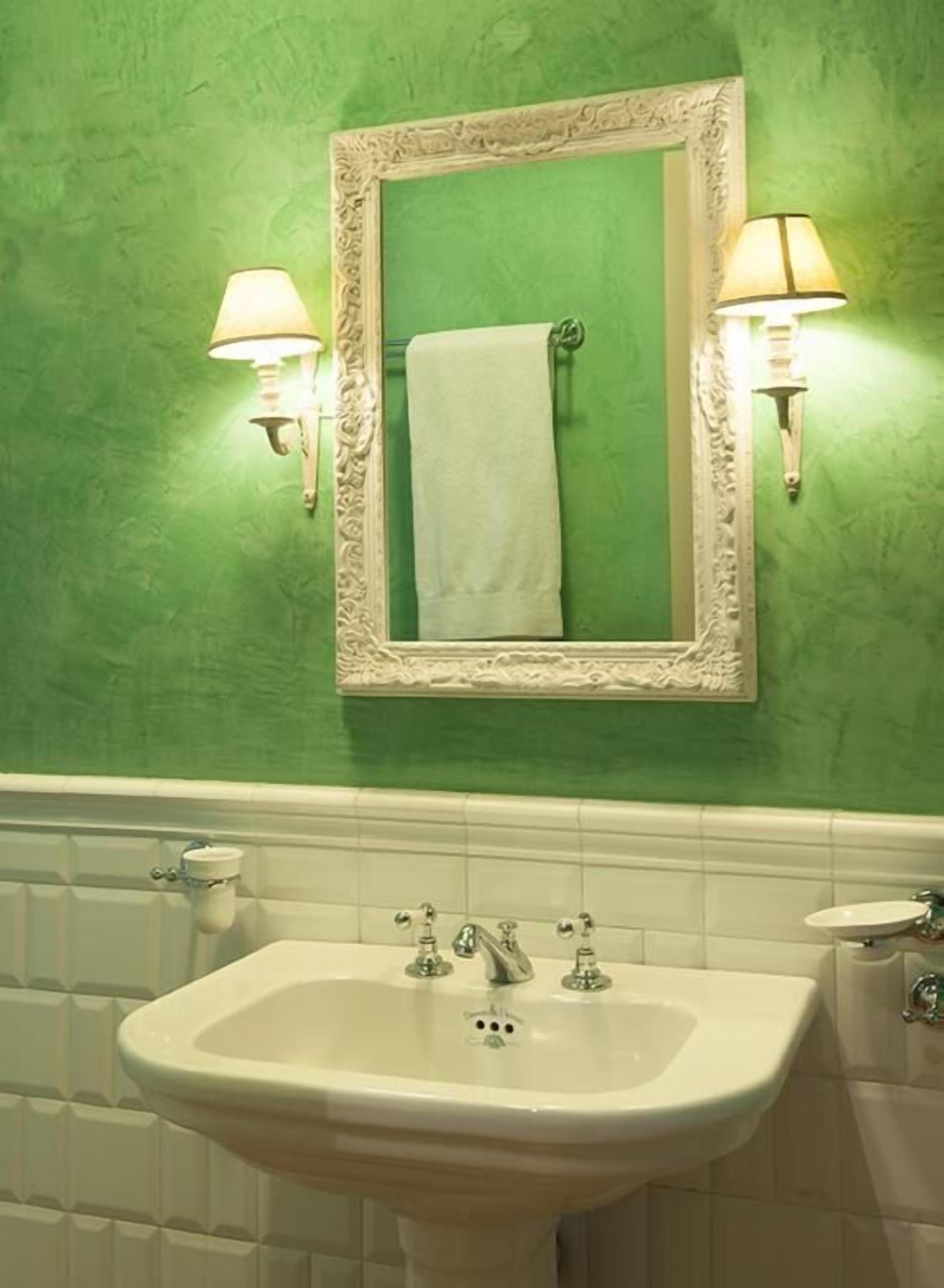 Ein Badezimmer mit grüner Wand, einem weißen Waschbecken und zwei Wandleuchten.