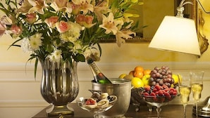 A table with a floral arrangement, a champagne bottle, fruit, and glasses. - Relais Vimercati (Crema)