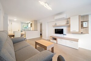 A modern living room with a grey sofa, wooden coffee table, TV, and built-in storage.