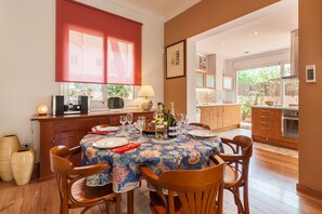 A dining area with a table set for four, a red window blind, and a kitchen in the background.
