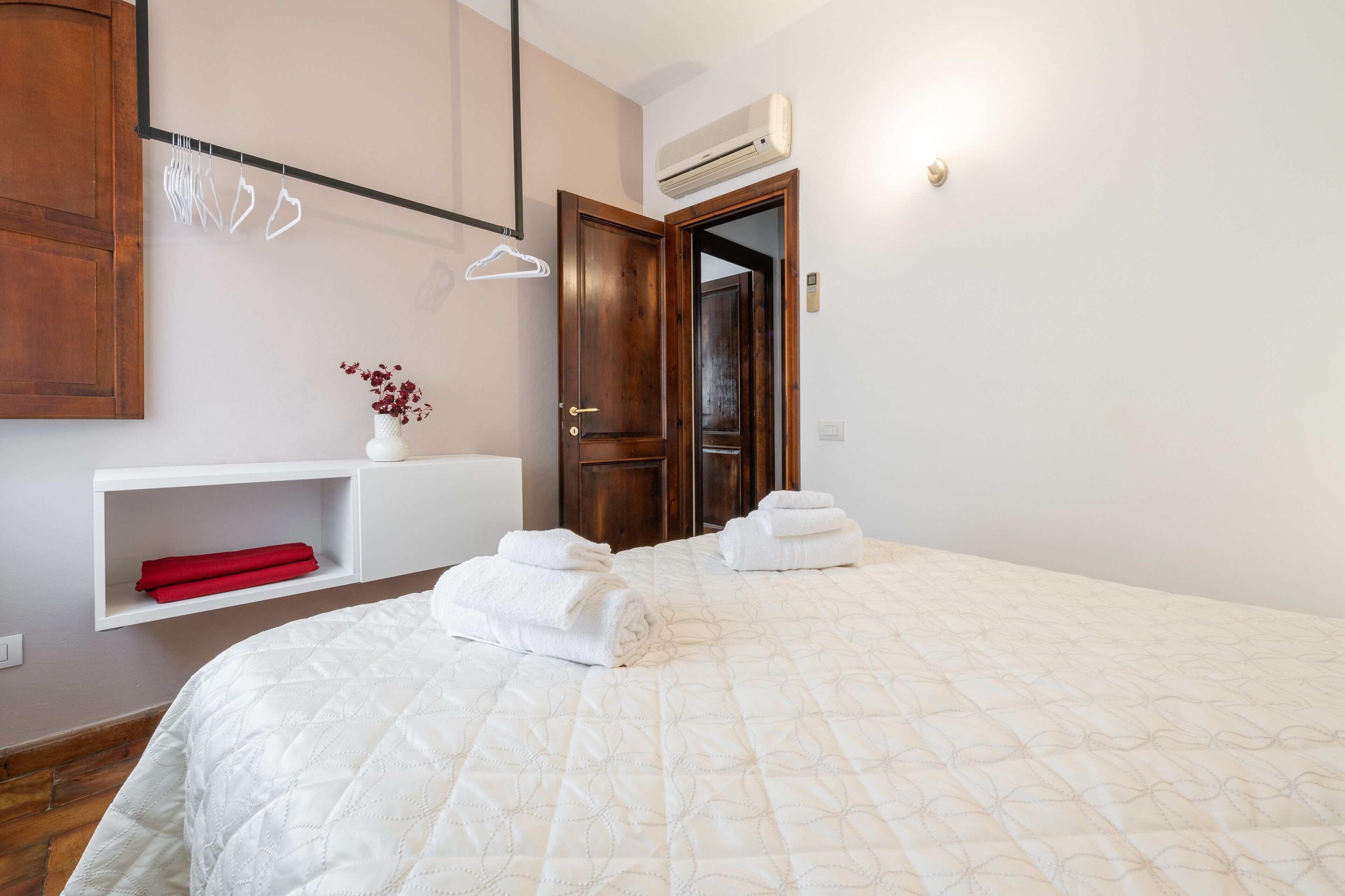 A bedroom with a bed, a wardrobe, a shelf with towels, and an air conditioning unit.