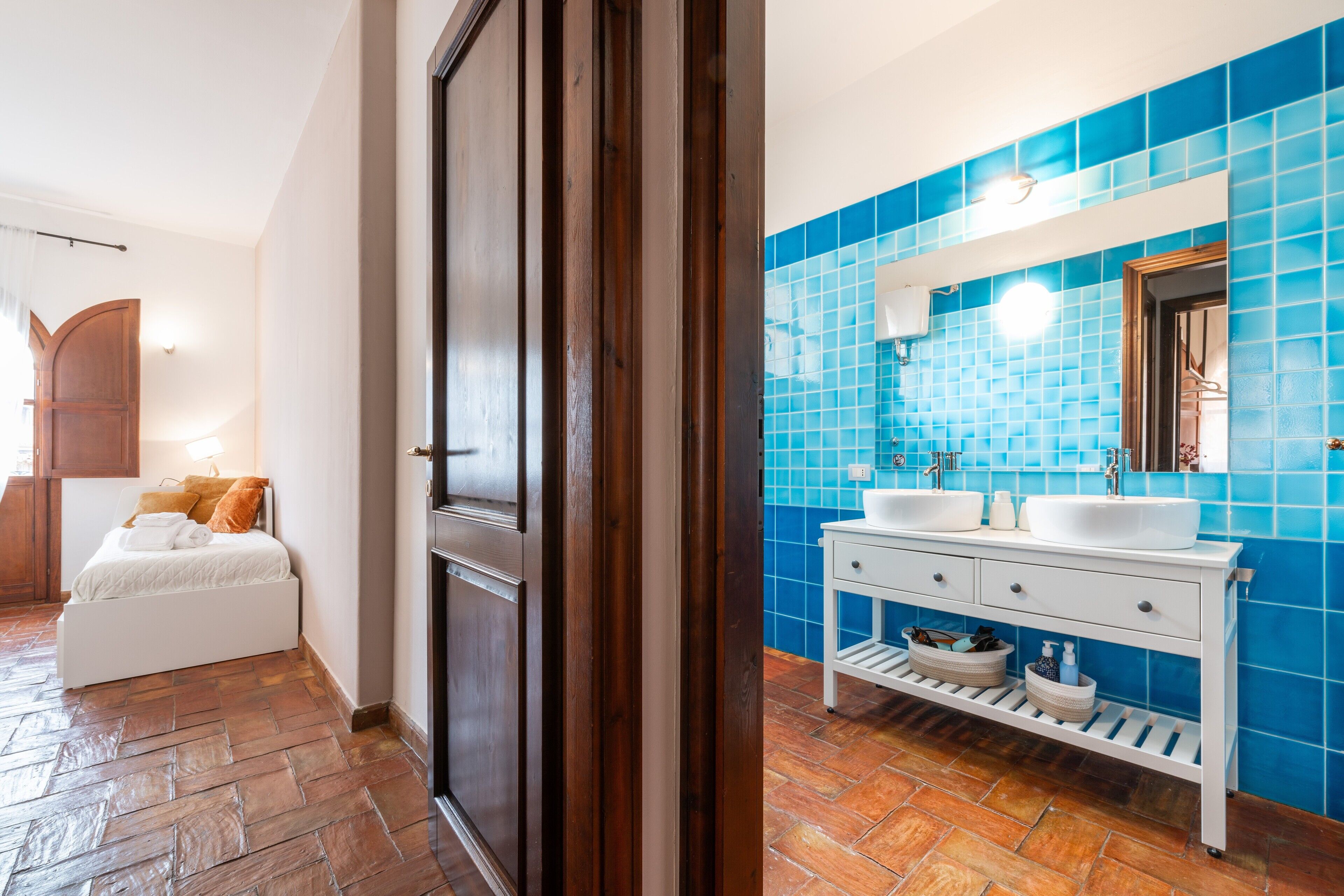Un bagno con piastrelle blu, un mobile lavabo bianco e un letto con testiera in legno.