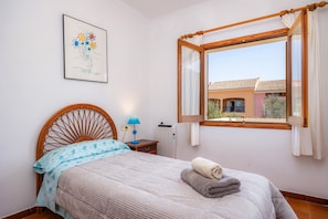 Une chambre à coucher avec un lit, une table de chevet, une lampe, une fenêtre avec des rideaux et un tableau encadré au mur.