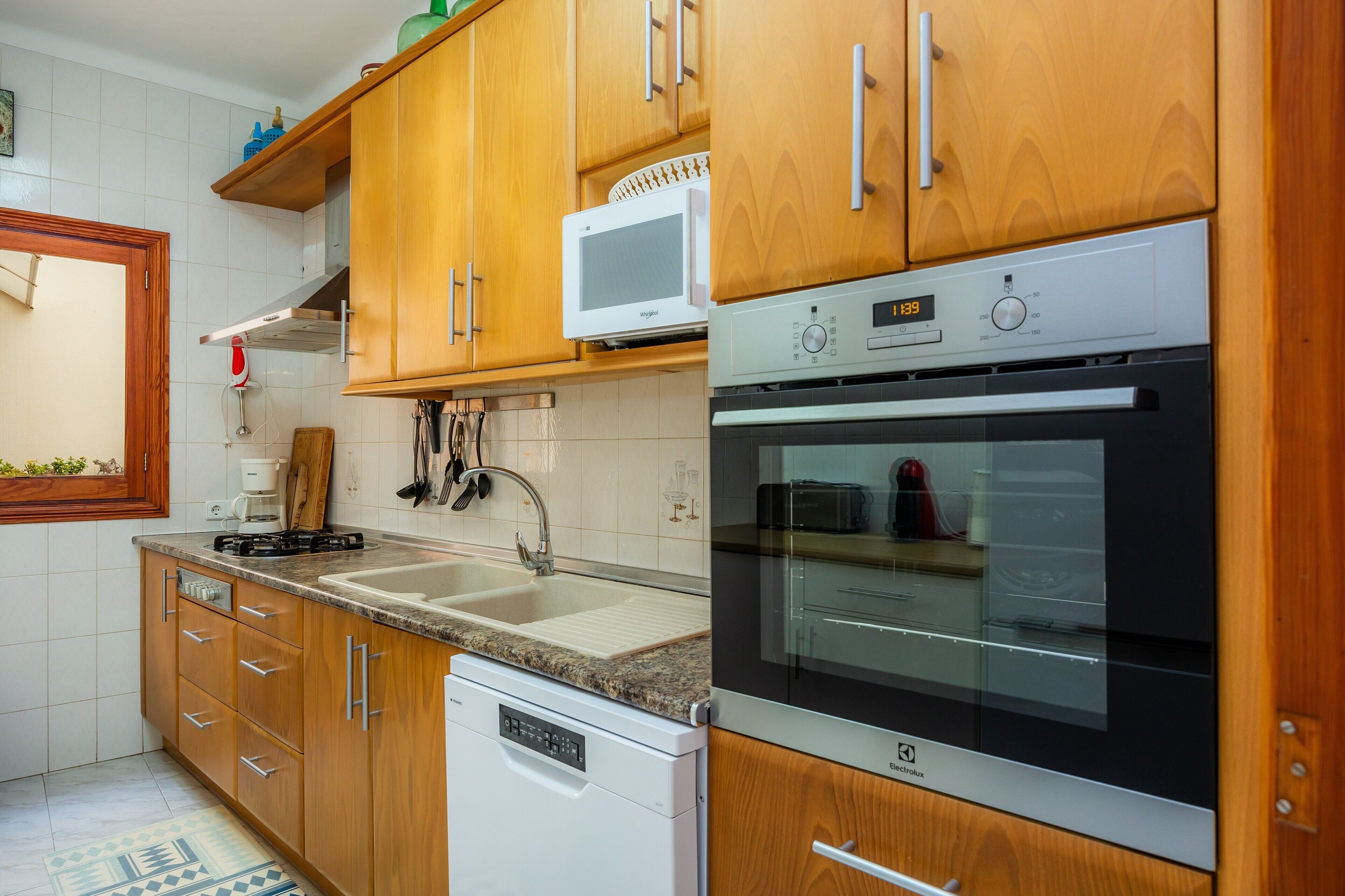 Una cocina con armarios de madera, microondas, horno, lavavajillas y fregadero.