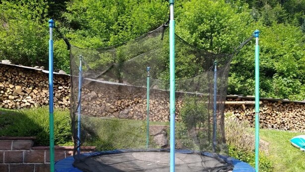 Un trampolín con red de seguridad, rodeado de un muro de piedra y follaje.