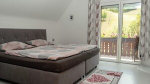 Un dormitorio con cama, mesita de noche, ventana con cortinas y vista a un jardín.