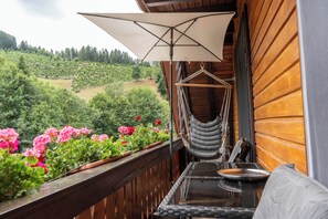 Un balcon avec un hamac, une table et une vue sur une colline boisée.