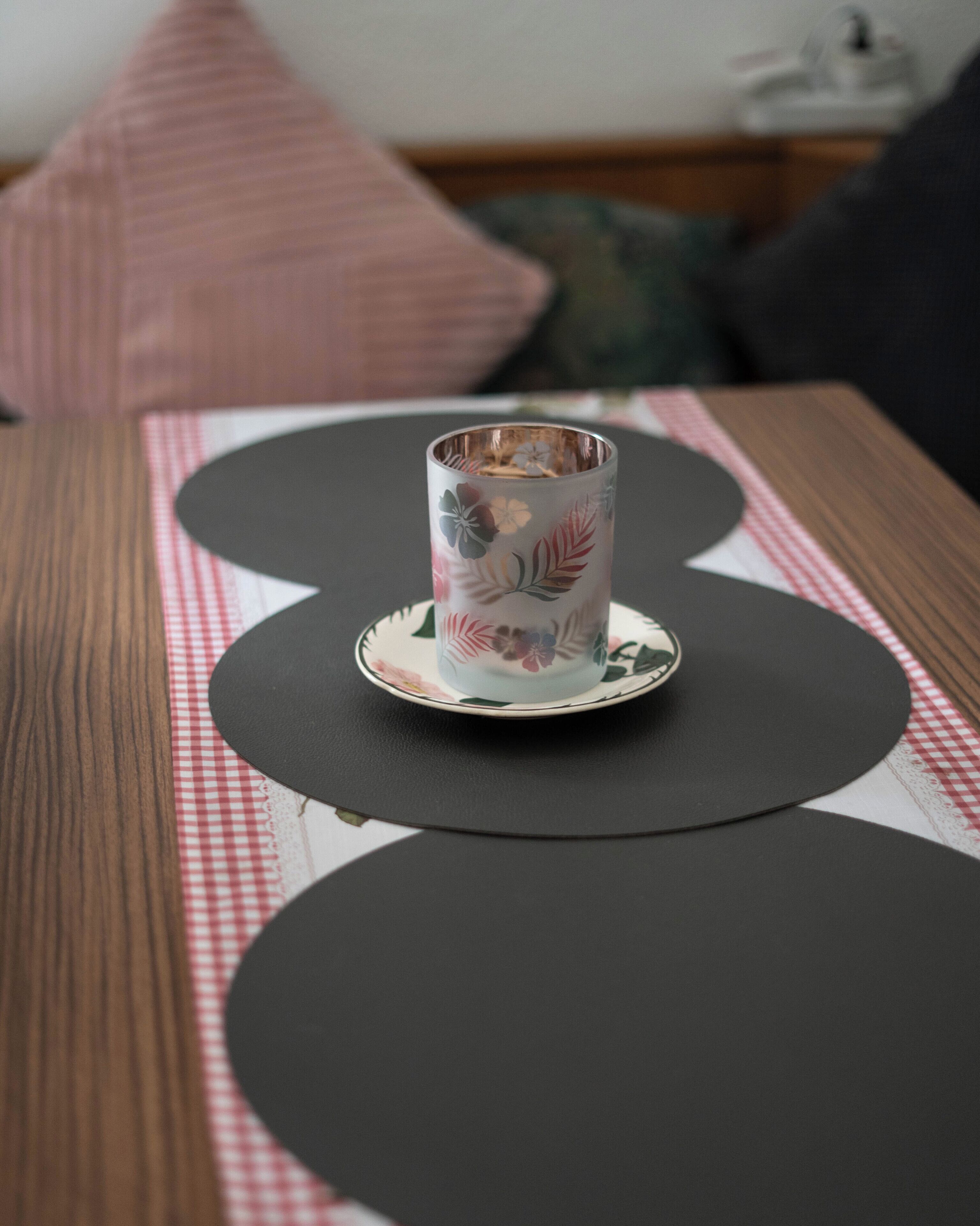 A table with a floral-patterned cup on a saucer, placed on a placemat with a checkered pattern.