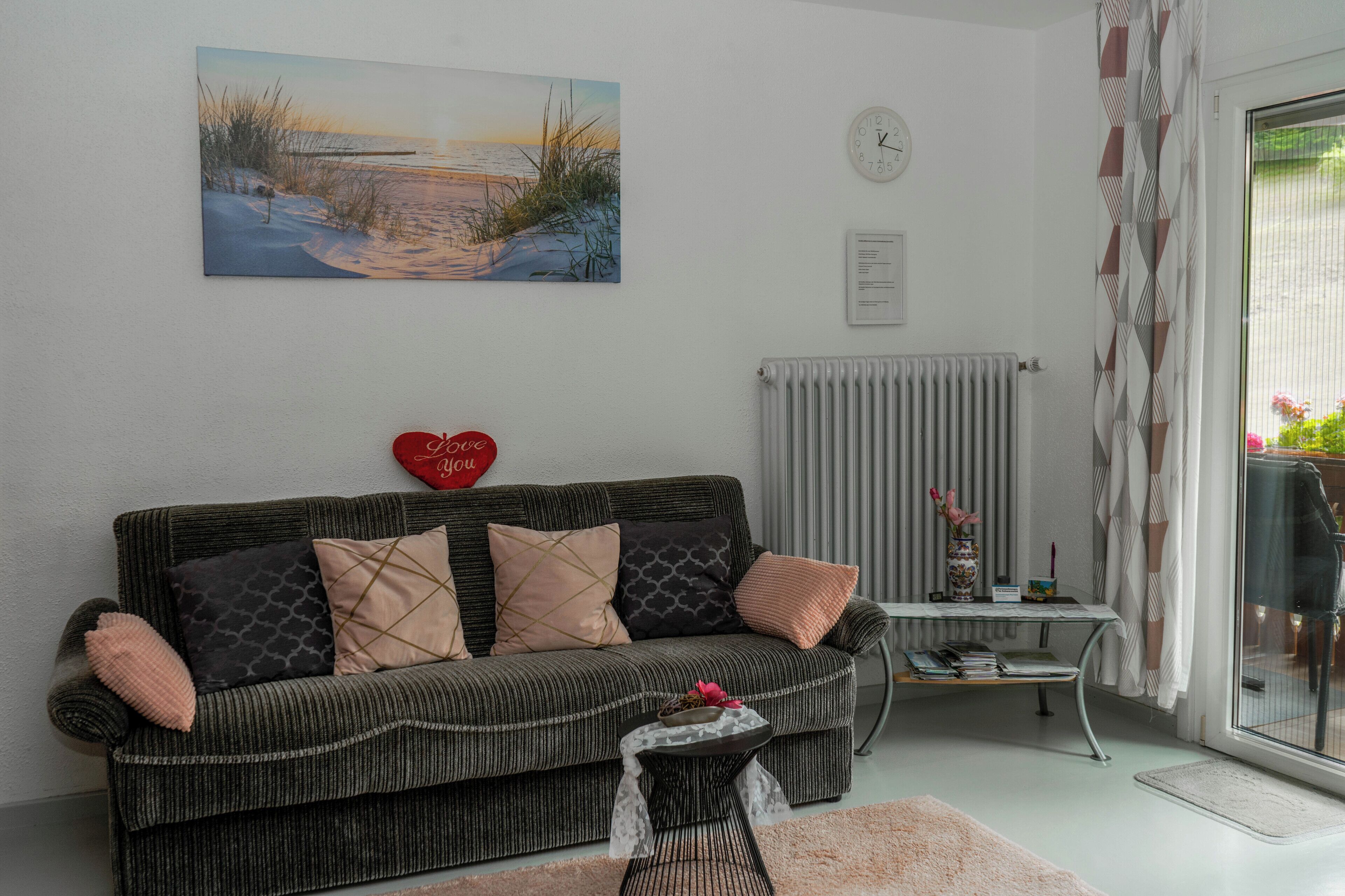 A living room with a sofa, a small table with a vase, a radiator, and a painting on the wall.