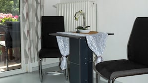 Una habitación con una mesa de comedor, dos sillas, un radiador y una ventana con vistas a árboles y flores.