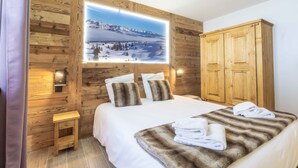 Ein Schlafzimmer mit einer Holzwand, einem Bett mit weißer Bettwäsche, einem Holzschrank und einem großen Fenster mit Blick auf die Berge.