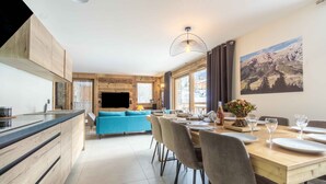 Eine moderne Küche mit Holzschnitzereien, ein Essbereich mit einem Holztisch und -stühlen sowie eine Wohnbereich mit einem blauen Sofa.