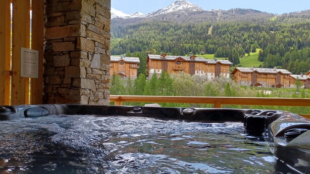 Ein Whirlpool mit Blick auf einen Berg und Holzhäuser im Hintergrund.