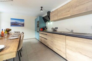 A modern kitchen with wooden cabinets, a black countertop, and a dining area with a wooden table set for four. - 'Chalet Pramaria - Apt L'Arcelle' with Mountain View, Wi-Fi and Air Conditioning (Lanslebourg Mont Cenis)